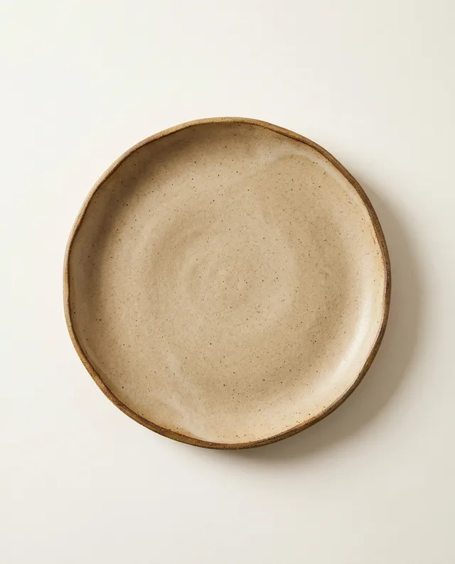Une assiette plate à l'émail sable, au bord d'argile plus sombre, vue de dessus.